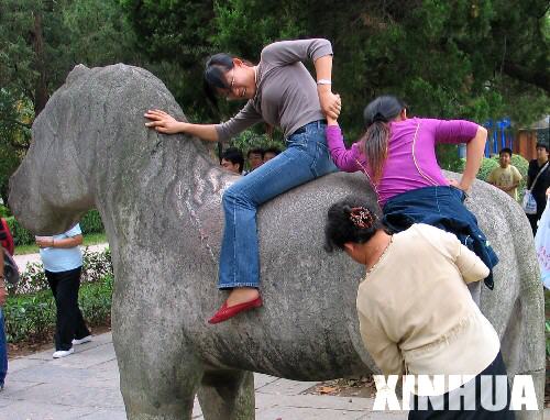 Tourists are trying to get onto a stone horse in a park